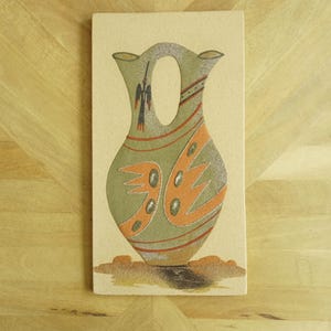 May include: Rectangular ceramic tile featuring a stylized vase design. The vase is primarily olive green with orange and silver accents, and a dark bird-like figure. The tile is set against a light beige background.