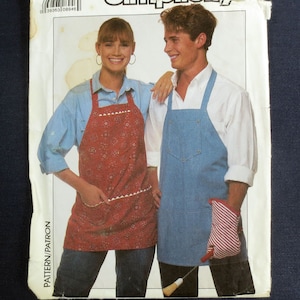 May include: Simplicity sewing pattern featuring aprons. One model wears a red patterned apron with white trim, and the other wears a blue denim apron. The pattern includes a matching oven mitt. The text "ONE SIZE" is visible.