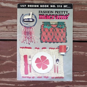 May include: A vintage Lily Design Book No. 213 titled Fashion Pretty macrame. The cover features illustrations of a blue macrame wall hanging, a green macrame handbag, and a white macrame placemat with a red floral plate, cutlery, and a mug.