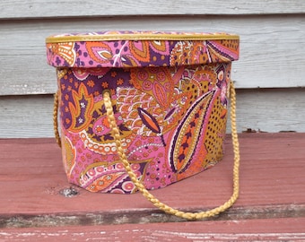 May include: A pink and orange paisley patterned hat box with a gold rope handle.