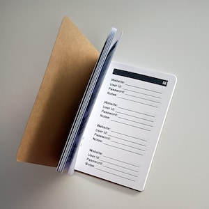 May include: A small, open notebook with a brown cover and white pages. The pages are printed with lines for website, user ID, password, and notes. The notebook is designed for organizing online account information.