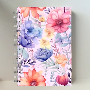 May include: A pink spiral bound notebook with a watercolor floral design featuring blue, pink, orange, and yellow flowers.