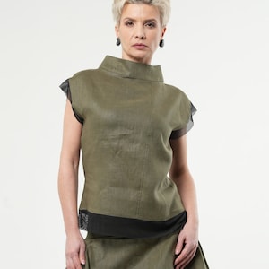 Puede incluir: Una mujer lleva una blusa de lino verde con ribetes negros y una falda de lino verde a juego. La blusa tiene cuello alto y mangas cortas.