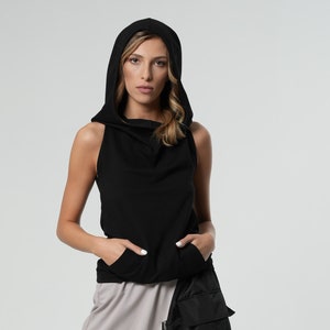 May include: A woman wearing a black sleeveless hoodie with a drawstring and a pair of gray harem pants with a black utility pocket and straps.
