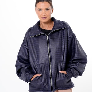 May include: A navy blue, oversized jacket with a textured, crocodile-like pattern. The jacket features a zip-up front, a stand-up collar, and two front pockets. The sleeves are long and slightly puffed. The model is wearing a black shirt and tan pants.