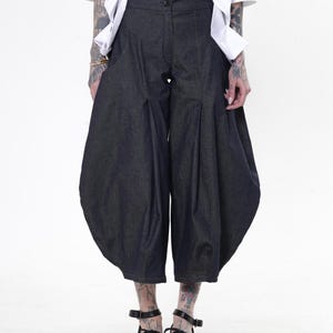 May include: Dark denim culottes with a unique, voluminous shape. These cropped pants feature a high waist and pleats, creating a distinctive silhouette. The pants are paired with black platform sandals. The model is wearing a white shirt.