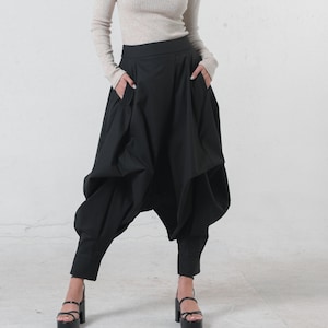 May include: A woman wearing a beige turtleneck sweater and black, loose-fitting pants with a unique, gathered design. She is wearing black platform sandals.