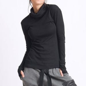May include: A black long-sleeved shirt with a mock neck and thumbholes. The shirt is made of a soft, stretchy fabric and has a relaxed fit.