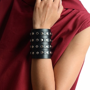 May include: A black leather bracelet with silver studs. The bracelet is wide and has multiple layers.