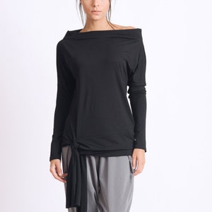 May include: A black long-sleeved shirt with a cowl neck and a knot at the waist. The shirt is paired with gray pants.