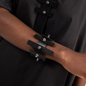 Puede incluir: Un collar gargantilla y una pulsera negros con tachuelas plateadas y m&uacute;ltiples correas. Las correas est&aacute;n conectadas por anillos met&aacute;licos.