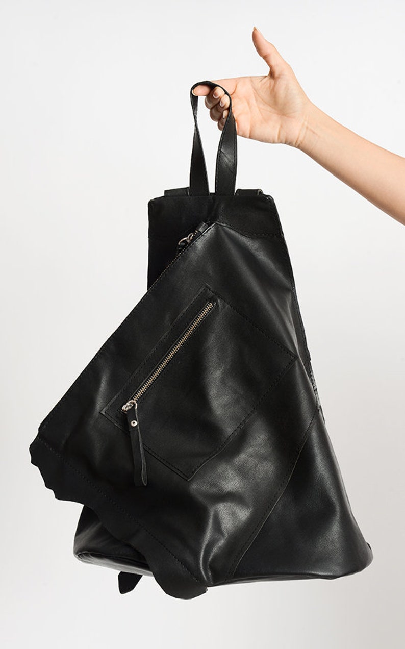 May include: A black leather backpack with a unique geometric design. The bag has a zippered pocket on the front and a top handle.