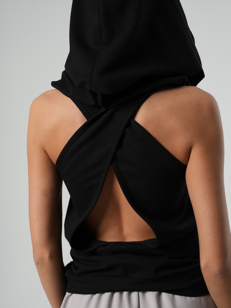 May include: Black hooded tank top with a criss-cross back design. The top has a large hood that can be worn up or down.