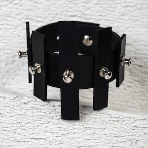 Puede incluir: Pulsera de cuero negro con tachuelas plateadas. La pulsera est&aacute; hecha de varias tiras de cuero que se unen con tachuelas plateadas.