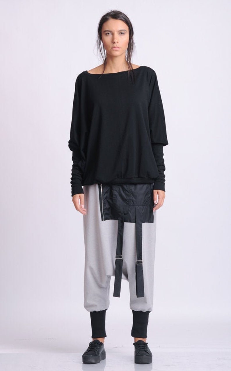 May include: A black long-sleeved top with a wide neckline and gray pants with a black panel and straps. The pants have black cuffs at the ankles, and the person is wearing black platform shoes. The outfit is modern and minimalist.