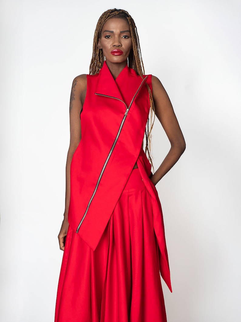 May include: A red sleeveless top with a long zipper down the front and a long red skirt. The top has a high collar and the skirt has a flowing design.