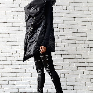 May include: A black puffer vest with a large, dramatic collar and a zipper closure. The vest is worn over a black long-sleeved shirt and black leggings. The person is wearing black platform boots.