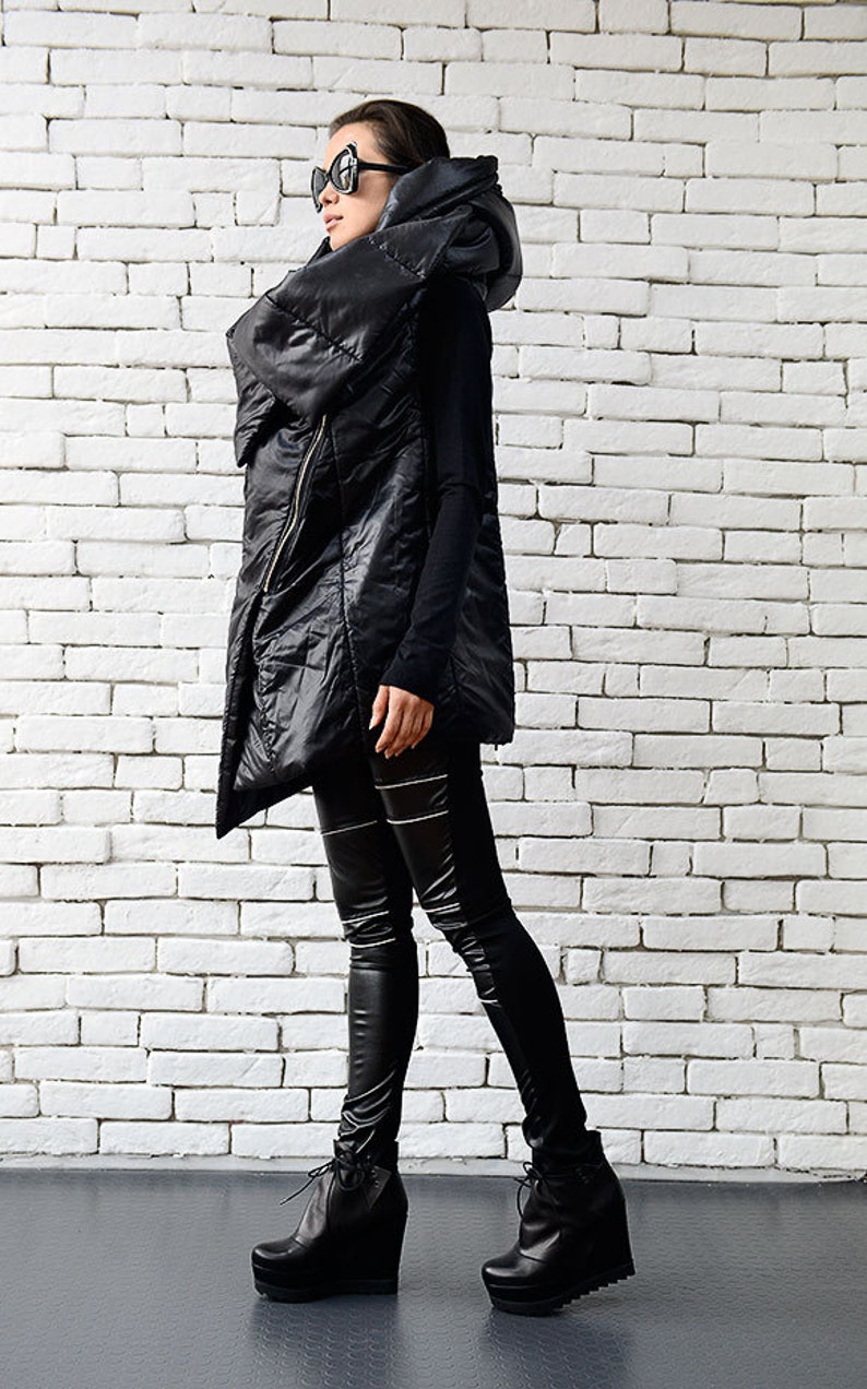 May include: A black puffer vest with a large, dramatic collar and a zipper closure. The vest is worn over a black long-sleeved shirt and black leggings. The person is wearing black platform boots.