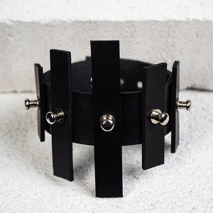 Puede incluir: Pulsera de cuero negro con tachuelas plateadas y un dise&ntilde;o geom&eacute;trico.