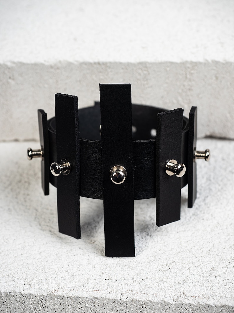 Puede incluir: Pulsera de cuero negro con tachuelas plateadas y un dise&ntilde;o geom&eacute;trico.