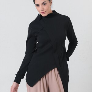 May include: A black mock neck shirt with a long sleeve and a diagonal seam detail. The shirt is asymmetrical and has a longer hem in the back.