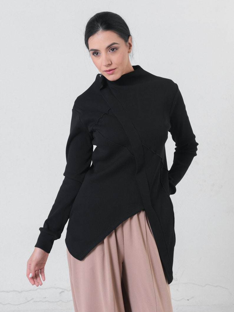 May include: A black mock neck shirt with a long sleeve and a diagonal seam detail. The shirt is asymmetrical and has a longer hem in the back.