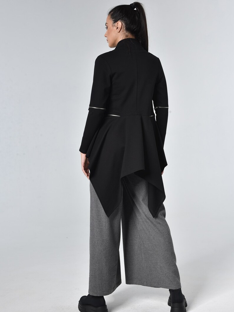 Puede incluir: Chaqueta negra de manga larga con cuello alto y bajo con volantes. La chaqueta tiene detalles de cremallera en las mangas y los lados.