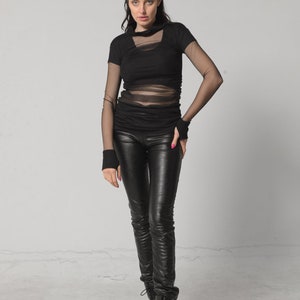 May include: A woman wearing a black mesh top with black leather trousers and black boots.