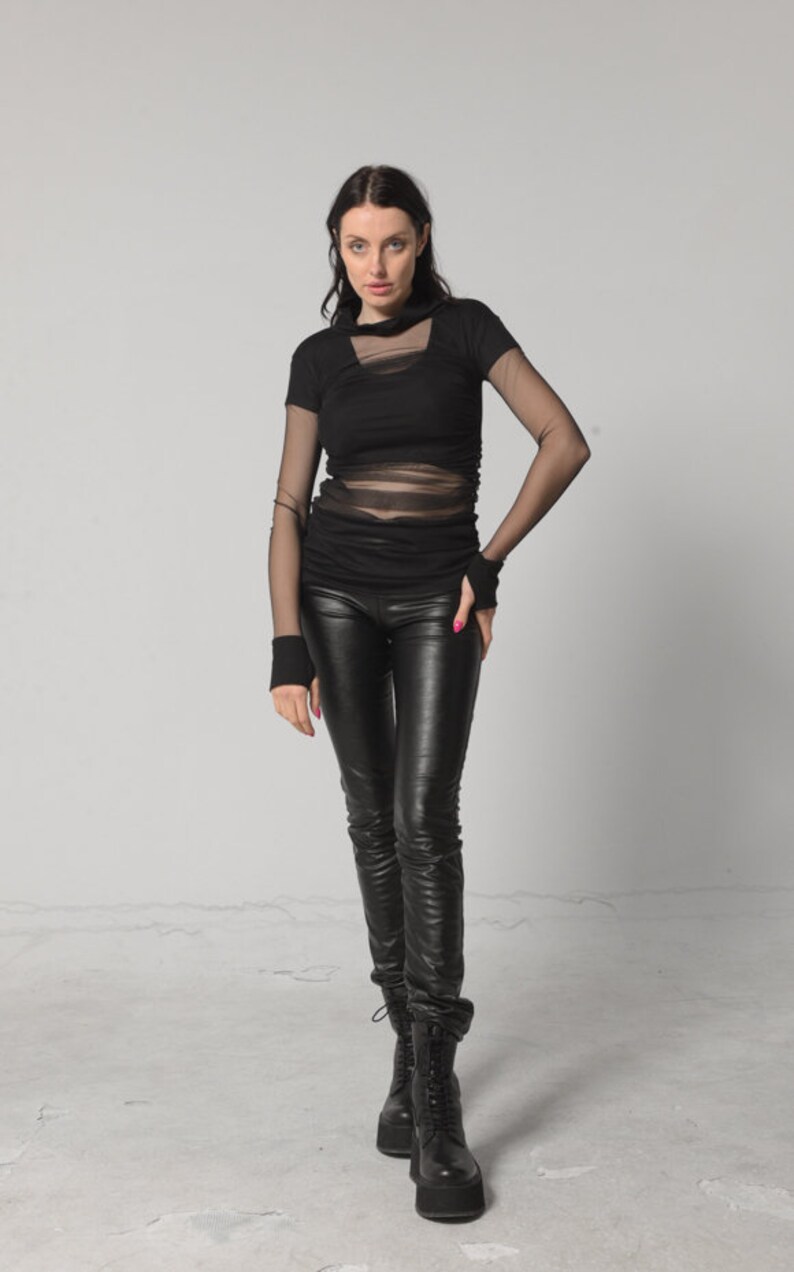May include: A woman wearing a black mesh top with black leather trousers and black boots.