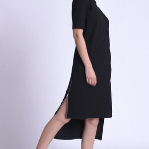 Puede incluir: Un vestido midi negro con un detalle de cremallera lateral. El vestido est&aacute; hecho de una tela suave y c&oacute;moda y tiene un ajuste holgado. La modelo lleva zapatillas negras con detalles blancos.