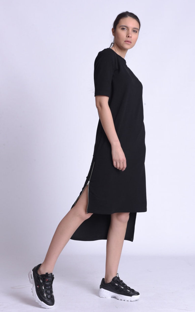 Puede incluir: Un vestido midi negro con un detalle de cremallera lateral. El vestido est&aacute; hecho de una tela suave y c&oacute;moda y tiene un ajuste holgado. La modelo lleva zapatillas negras con detalles blancos.
