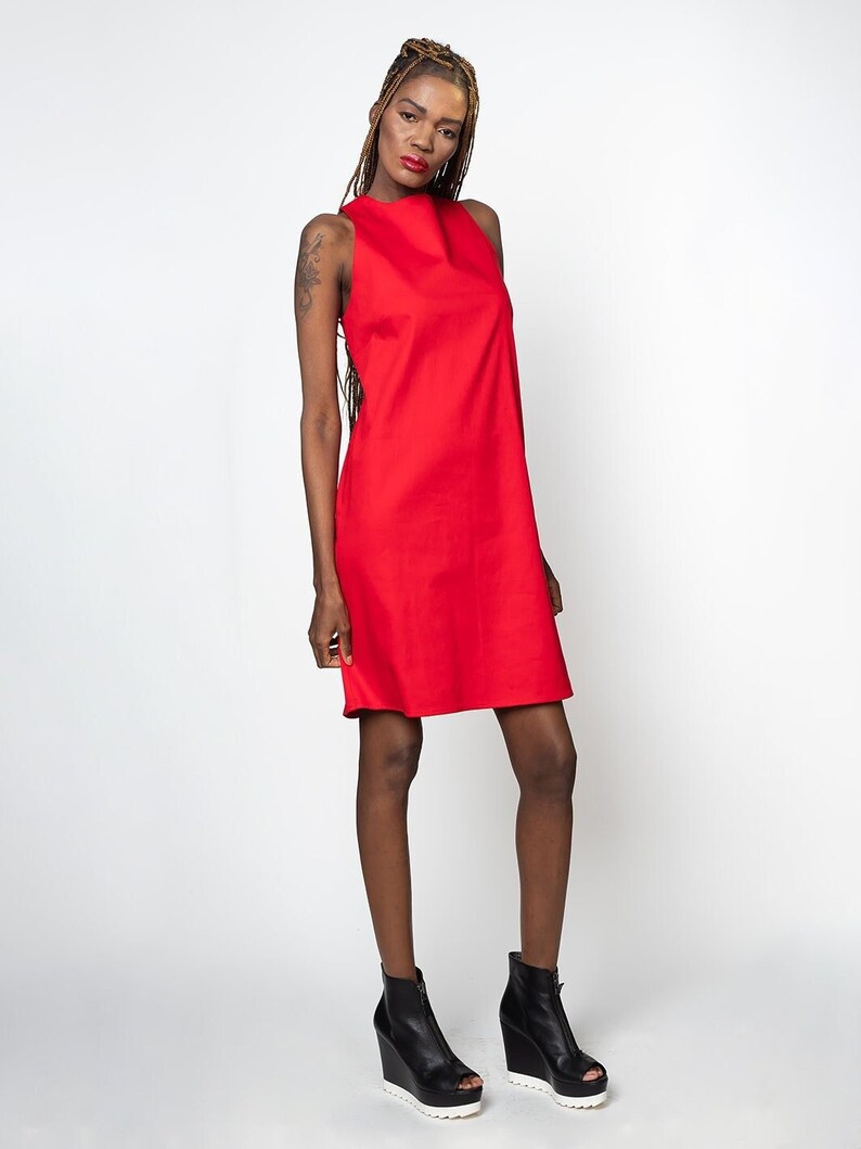 May include: A sleeveless red dress with a high neckline. The dress is knee-length and has a straight silhouette. The model is wearing black wedge heels.