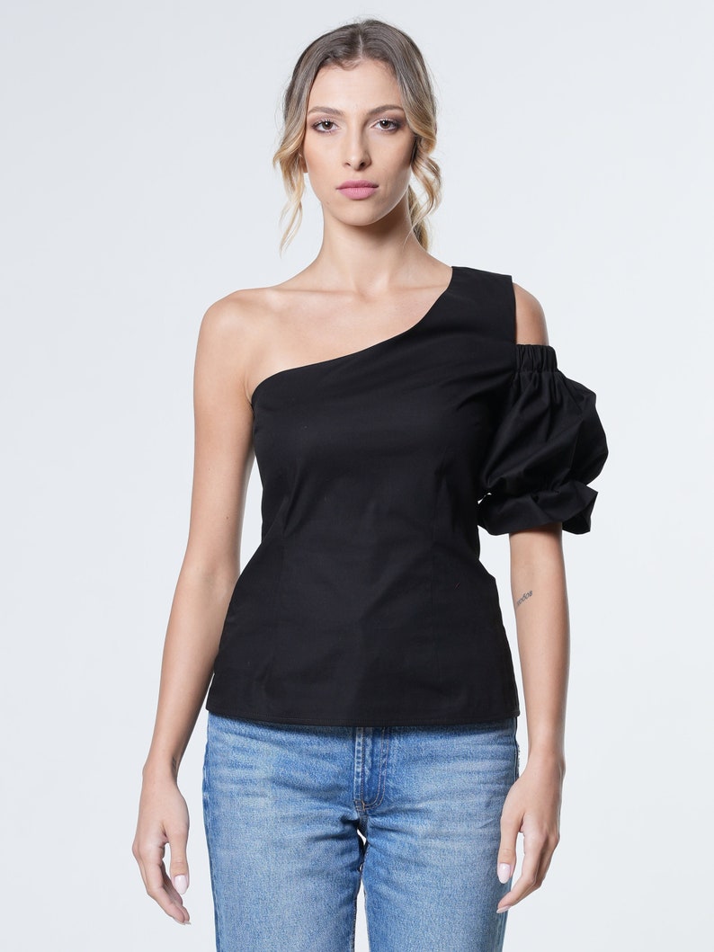 May include: A black one-shoulder top with a puffed sleeve. The top is made of a soft, lightweight fabric and has a fitted silhouette.