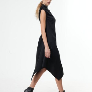 K&ouml;nnte beinhalten: Ein schwarzes, &auml;rmelloses Kleid mit hohem Kragen und asymmetrischem Saum. Das Kleid ist am Oberk&ouml;rper figurbetont und weitet sich zum Saum hin.