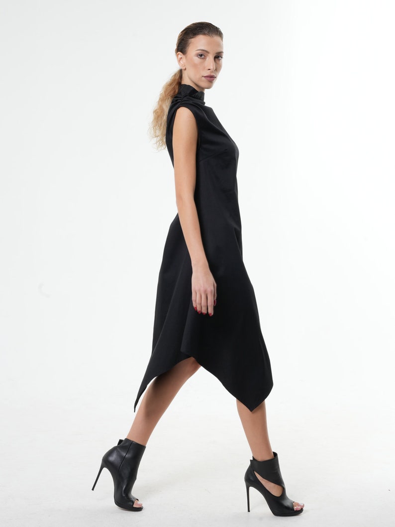 K&ouml;nnte beinhalten: Ein schwarzes, &auml;rmelloses Kleid mit hohem Kragen und asymmetrischem Saum. Das Kleid ist am Oberk&ouml;rper figurbetont und weitet sich zum Saum hin.