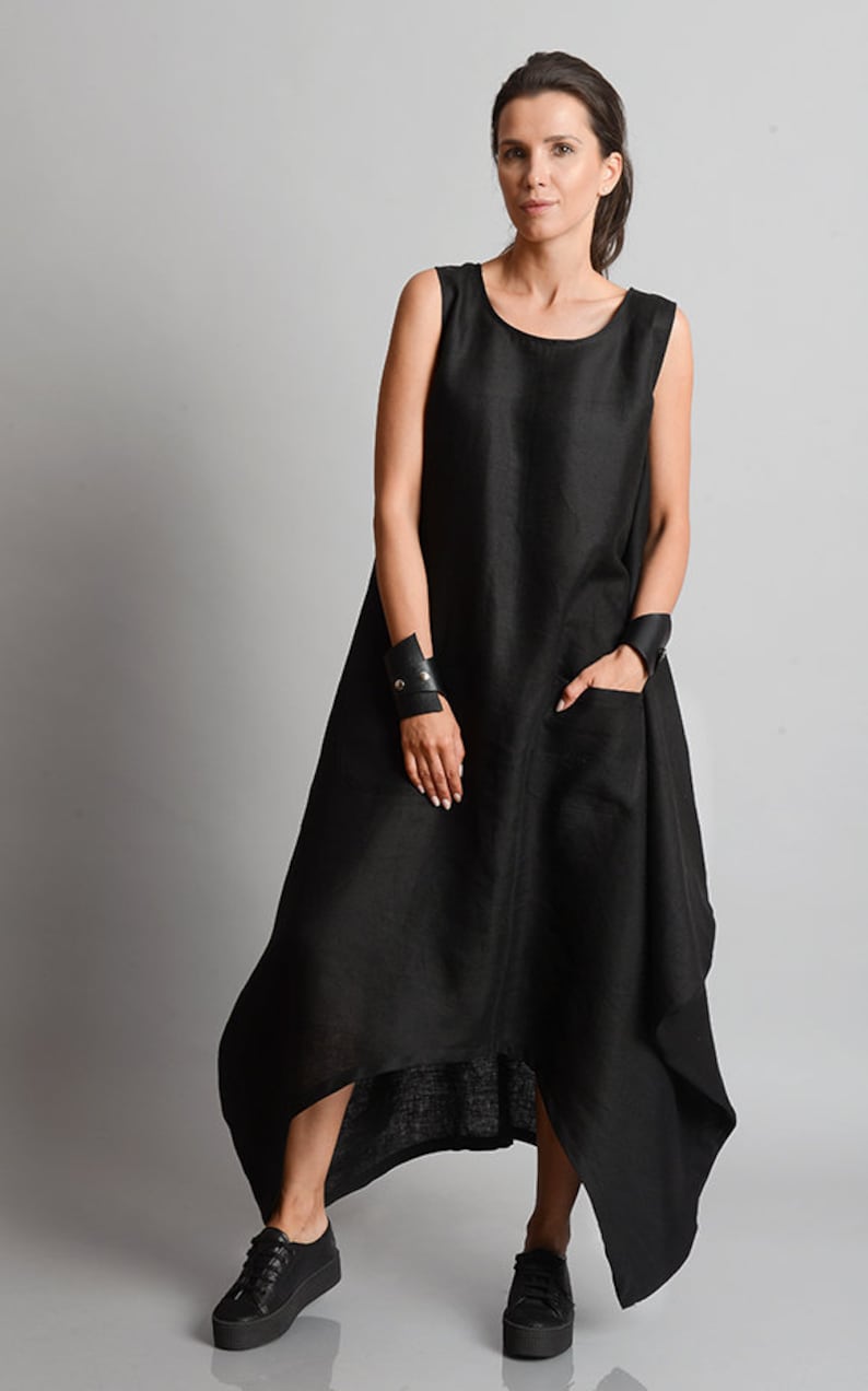 May include: A black sleeveless linen dress with a high low hemline and a pocket on the left side. The dress is asymmetrical and has a relaxed fit.