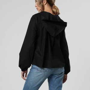 Puede incluir: Una chaqueta negra con capucha, mangas largas y un corte holgado. La chaqueta est&aacute; hecha de un tejido ligero y tiene una capucha con cord&oacute;n.