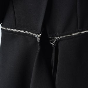 Puede incluir: Primer plano de un vestido negro con dos cremalleras plateadas que bajan por el frente.