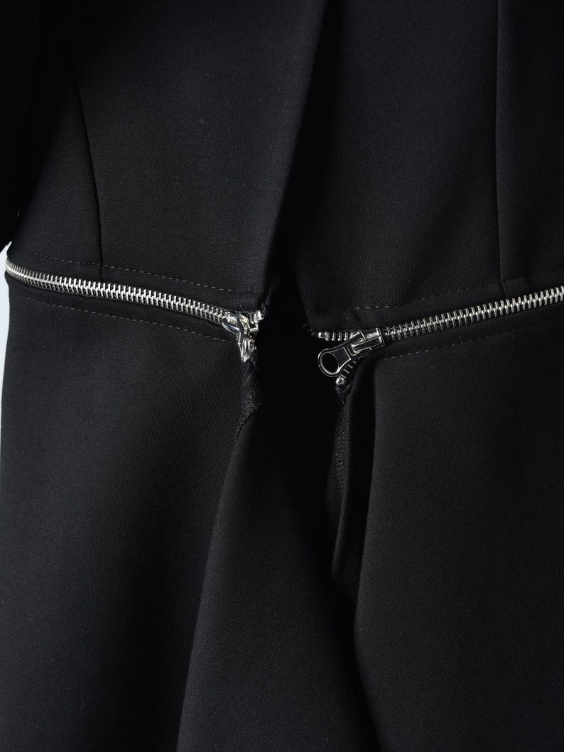 Puede incluir: Primer plano de un vestido negro con dos cremalleras plateadas que bajan por el frente.