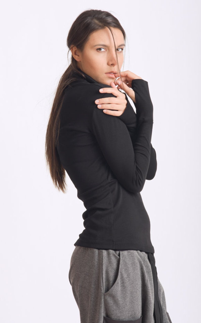 May include: A woman wearing a black long-sleeved shirt with a mock neck and gray sweatpants.