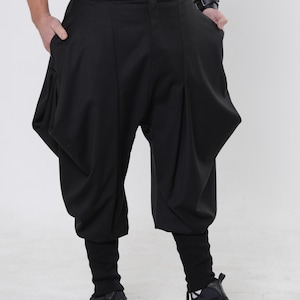 Puede incluir: Pantalones negros de estilo harén con un diseño voluminoso único. Los pantalones tienen cintura alta, cierre de botón y bolsillos profundos. Las perneras inferiores son ajustadas, y el modelo lleva zapatillas negras.
