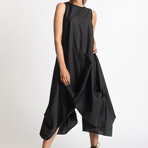 Peut inclure: Une robe noire sans manches avec un design drap&eacute; et une coupe ample. La robe est faite d'un tissu l&eacute;ger et a une silhouette fluide. Le mannequin porte la robe avec des sandales &agrave; plateforme noires.