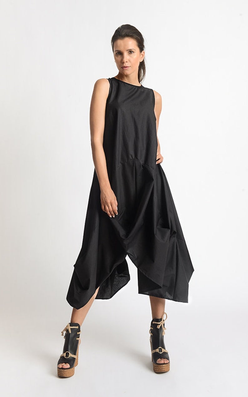 Peut inclure: Une robe noire sans manches avec un design drap&eacute; et une coupe ample. La robe est faite d'un tissu l&eacute;ger et a une silhouette fluide. Le mannequin porte la robe avec des sandales &agrave; plateforme noires.
