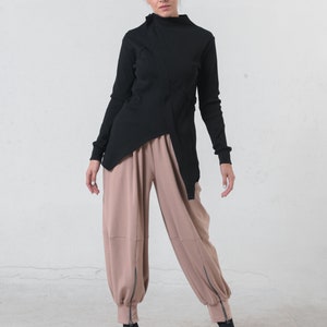 May include: A black mock neck shirt with a long sleeve and a diagonal seam detail. The shirt is paired with loose-fitting, light brown pants with zippered ankles.