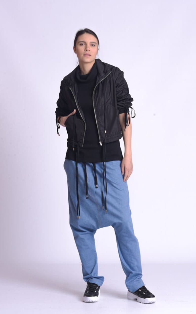 May include: A woman wearing a black zip-up jacket with a black turtleneck shirt and blue denim pants with a drawstring waist.