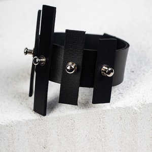 Puede incluir: Pulsera de cuero negro con tachuelas plateadas y dise&ntilde;o geom&eacute;trico.