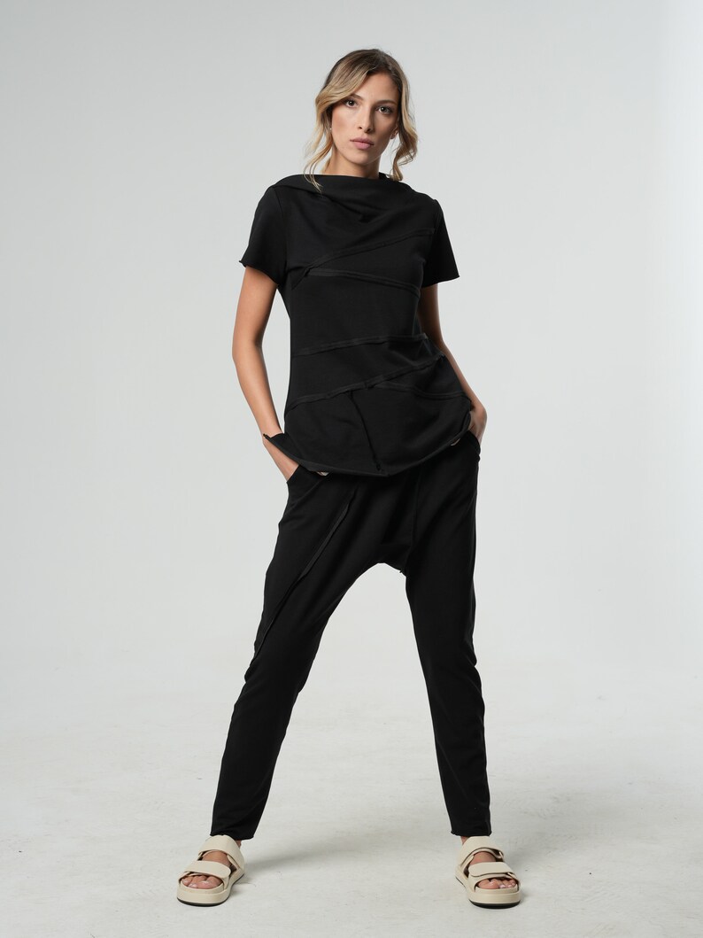 May include: A black, short-sleeved top with a cowl neck and a layered design. The top is paired with black, loose-fitting pants and white sandals.