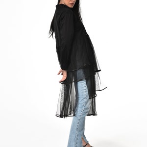 May include: A black long-sleeved shirt with a sheer overlay and a ruffled hem. The shirt is paired with light blue jeans and black platform sandals.