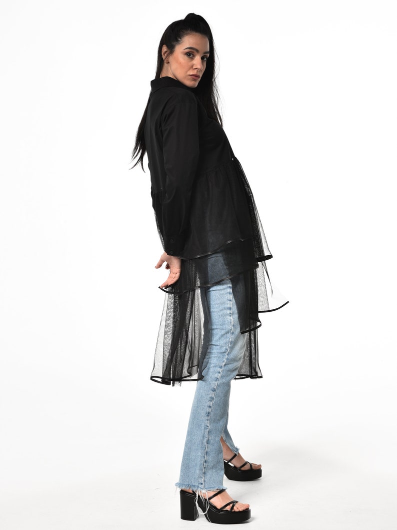 May include: A black long-sleeved shirt with a sheer overlay and a ruffled hem. The shirt is paired with light blue jeans and black platform sandals.