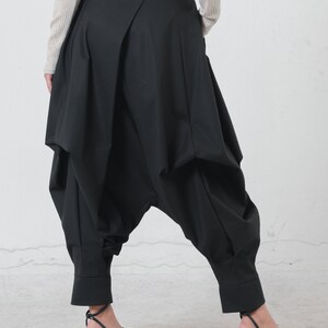 May include: Black, wide-leg pants with a unique, gathered design. The pants have a high waist and a loose, flowing fit.